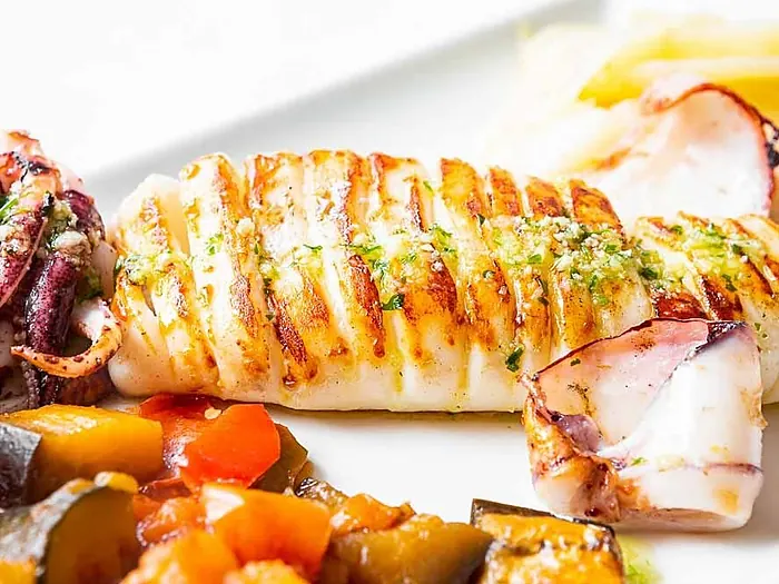 Calamar a la plancha con verduras servido en plato blanco